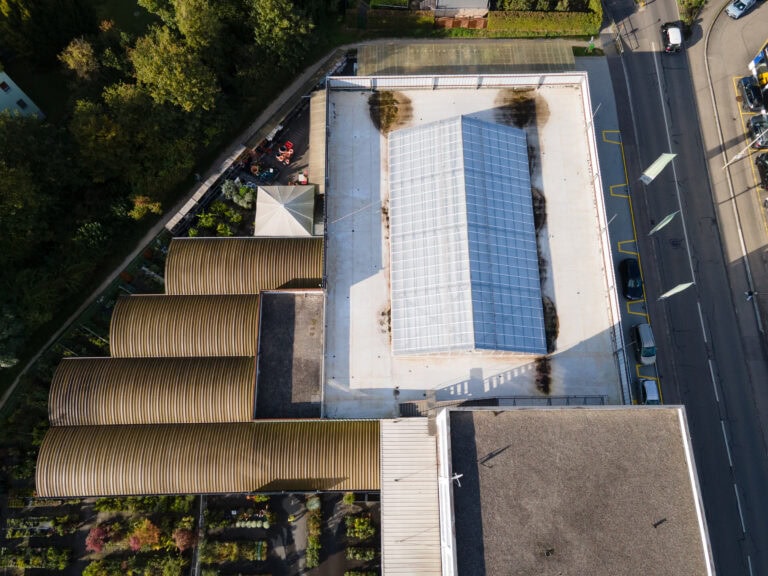 Luftaufnahme eines Gewächshauskomplexes mit einem großen glasüberdachten Zentralgebäude, mehreren Runddachkonstruktionen, angrenzenden Gärten und einer nahe gelegenen Straße mit geparkten Autos - ideale Lebensräume in bewirtschafteten Gewerbeliegenschaften.