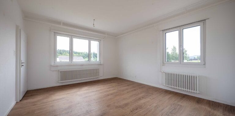 Helle, leere Räume ideal für die Verwaltung oder Vermietung-weiße Wände, große Fenster mit Blick ins Grüne, zwei Heizkörper und helles Holzparkett schaffen luftige Lebensräume voller Licht.