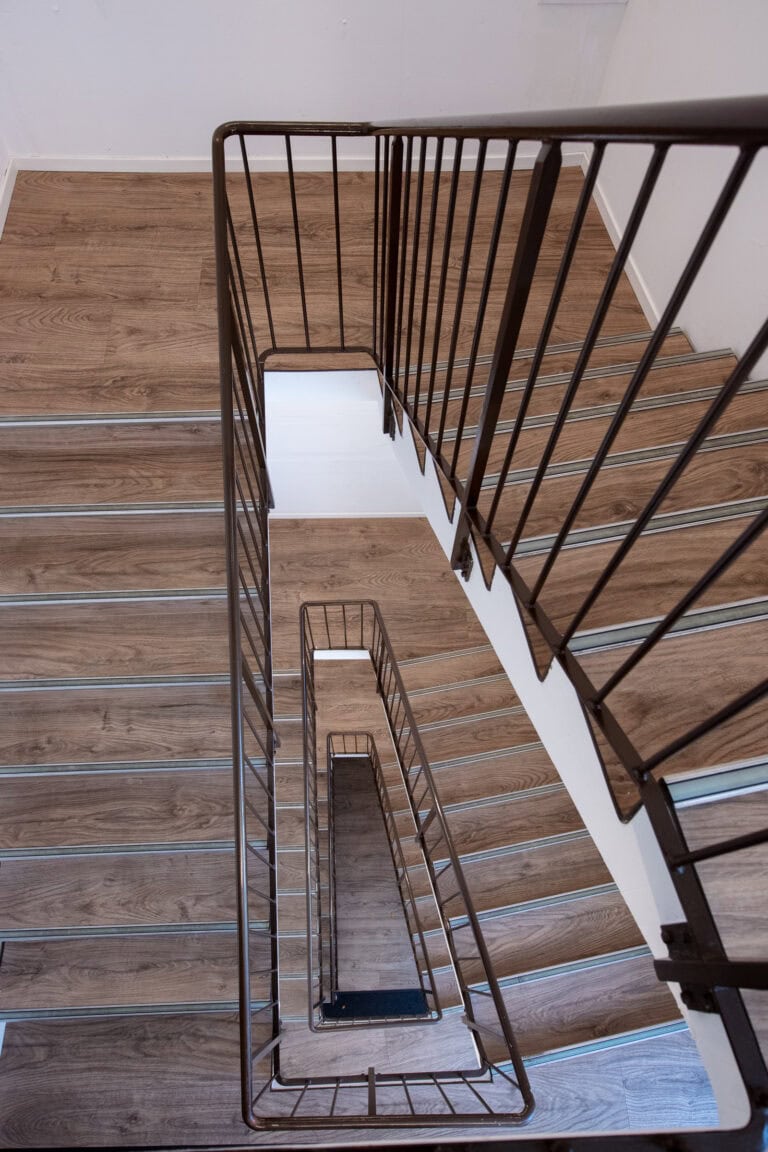 Draufsicht auf eine moderne Innentreppe mit Holzstufen und dunklem Metallgeländer, die ein rechteckiges Spiralmuster bildet - perfekt für die Verwaltung oder Vermietung von exklusiven Gewerbeliegenschaften über mehrere Etagen.
