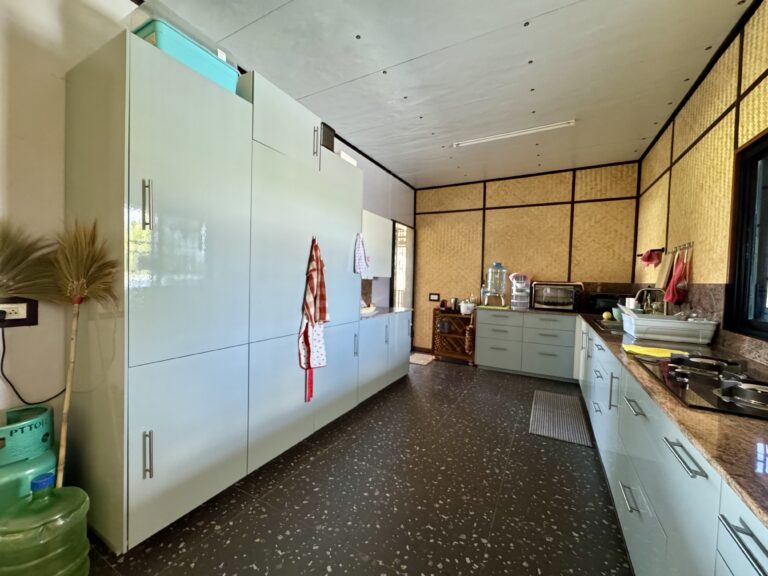 Moderne Küche mit hellgrünen Schränken, schwarz gesprenkeltem Bodenbelag, Arbeitsplatten, einer großen Wasserflasche und an Schrankgriffen hängenden Utensilien. Bambusgemusterte Wände und ein großes Fenster füllen den Raum mit natürlichem Licht.